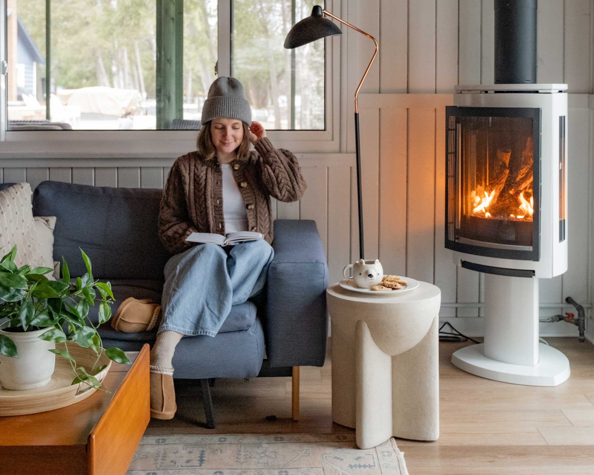 woman sitting on couch next to fire place reading a book